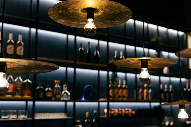 Brass cymbal lamps glowing over the bottle shelves